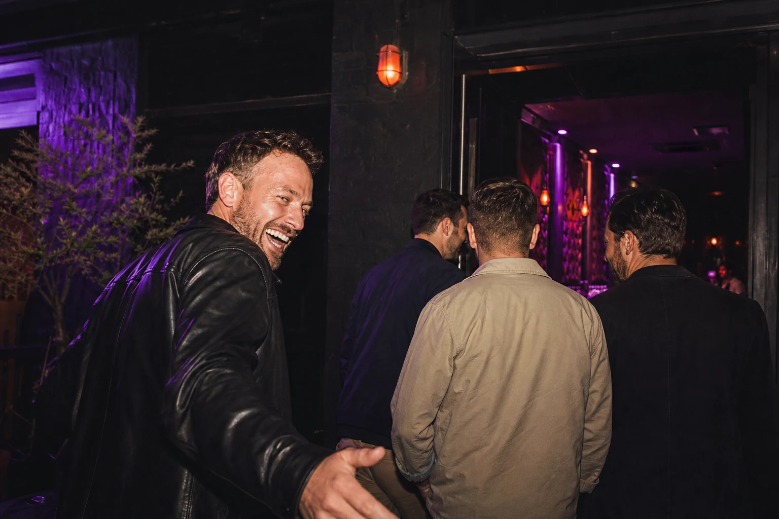 Direct-flash editorial photograph of friends entering a compact nightlife venue in deep violet and orange