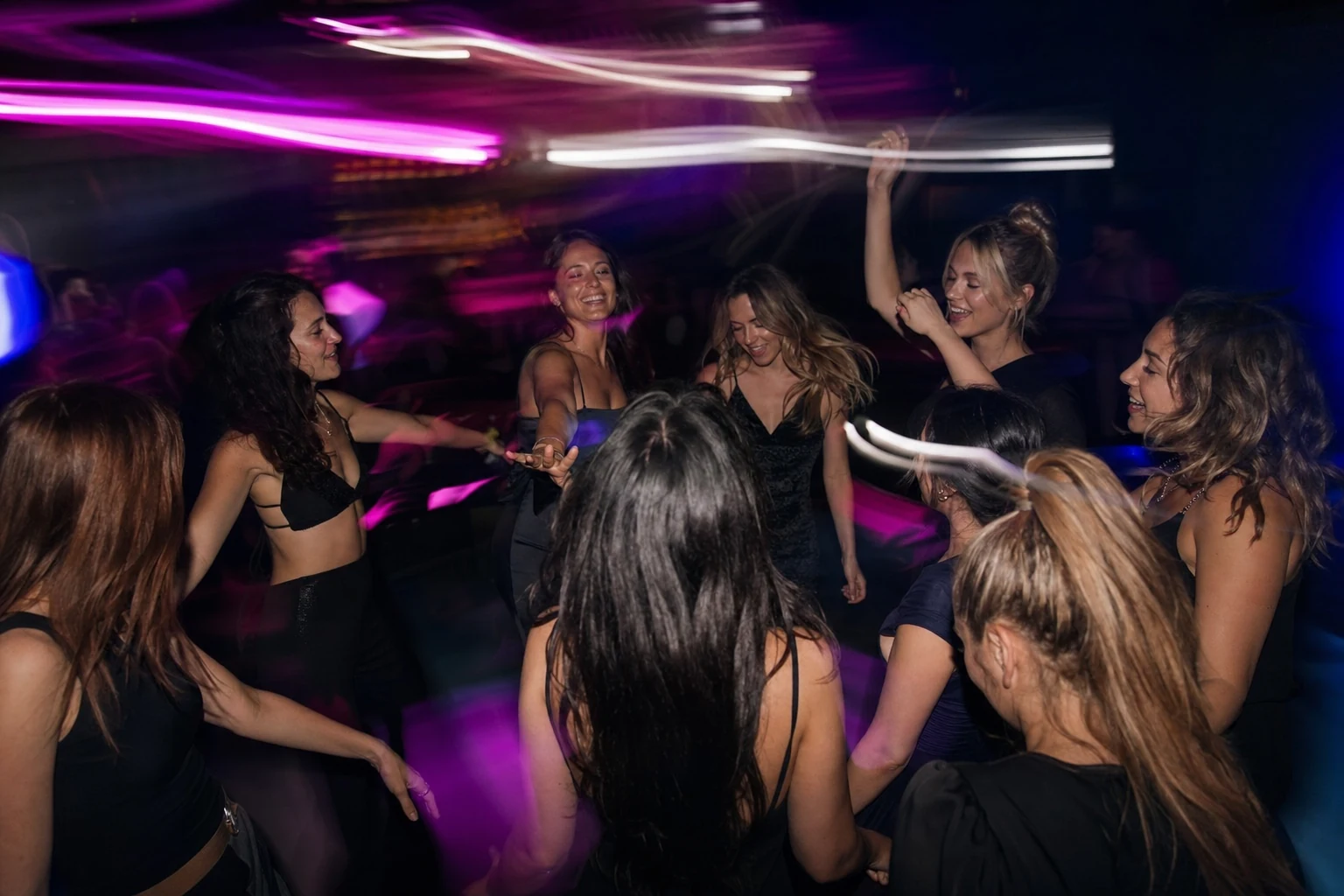 Slow-shutter dance-floor photograph of friends forming a loose circle around the bride