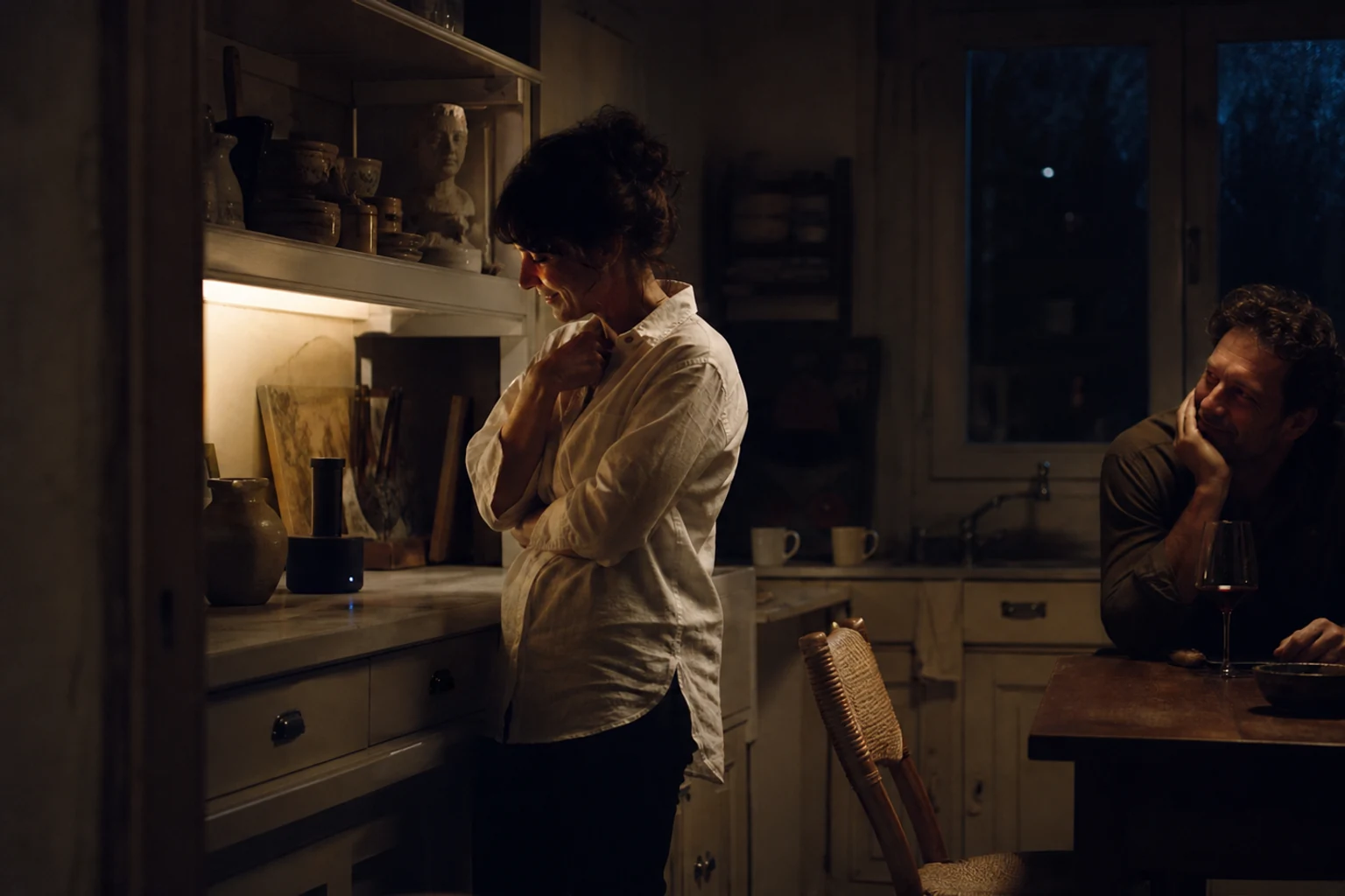 Private nighttime kitchen listening moment in wine, warm gray, and ivory light